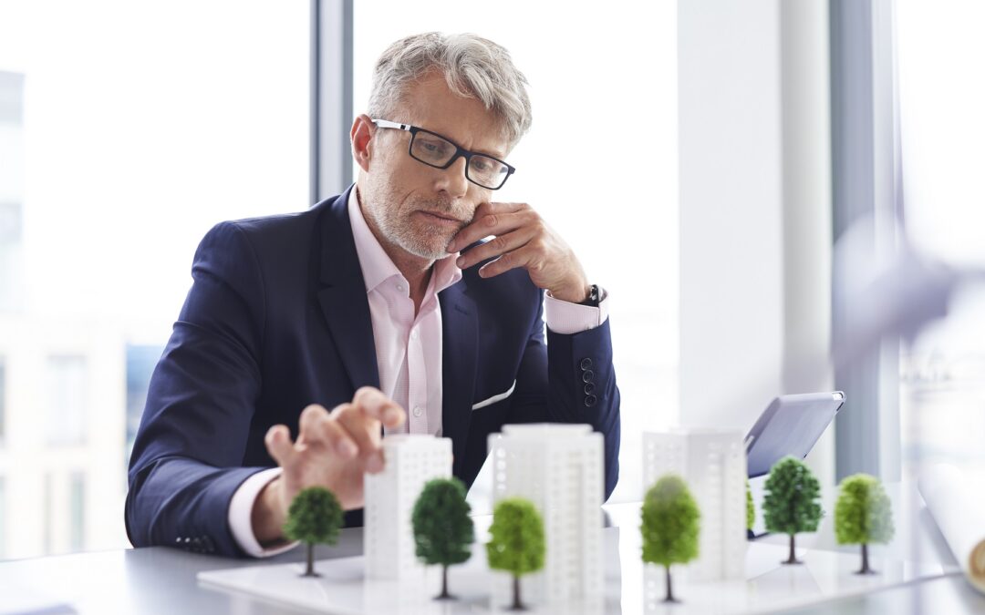 Un homme en costume observe attentivement une maquette de bâtiments et d’arbres.