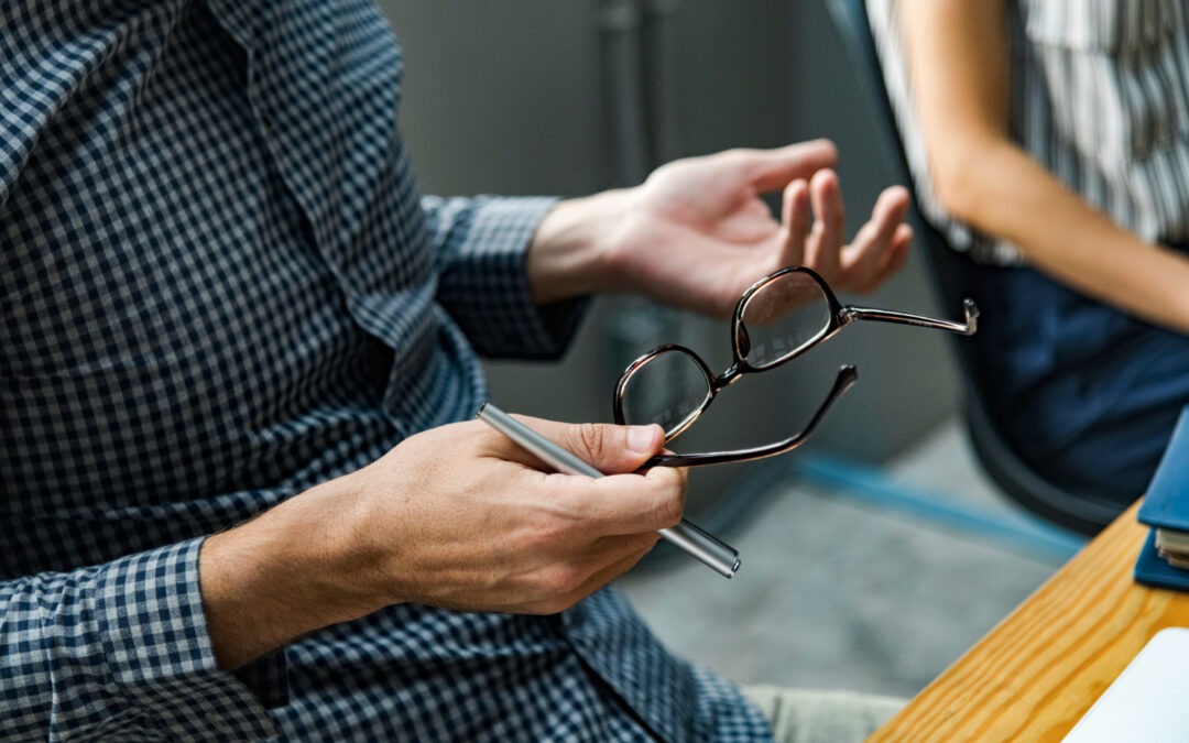 mains d'un professionnel tenant une paire de lunettes et un stylo