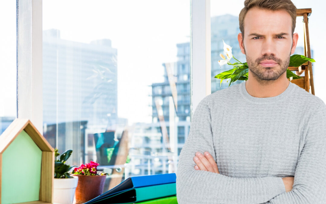 Un homme au regard sérieux À ses côtés, une petite maison en bois et des dossiers de travail