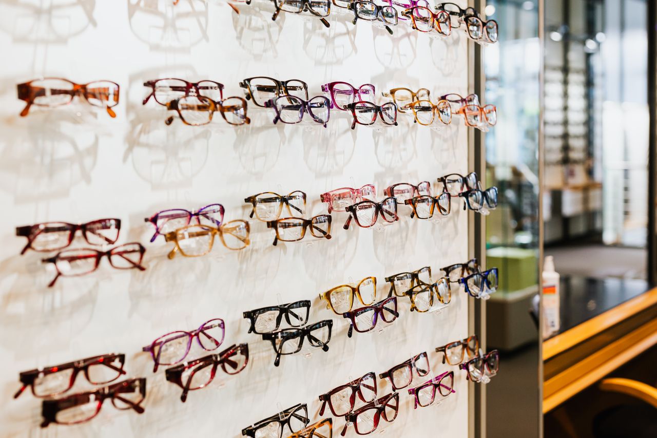 un grand présentoir mural d'opticien exposant de nombreuses montures de lunettes de vue variées, rangées sur plusieurs rangées