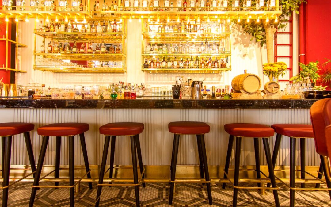 un comptoir de bar chic et moderne aligné de tabourets hauts au siège rouge, surplombé d'étagères dorées et lumineuses chargées de bouteilles de spiritueux