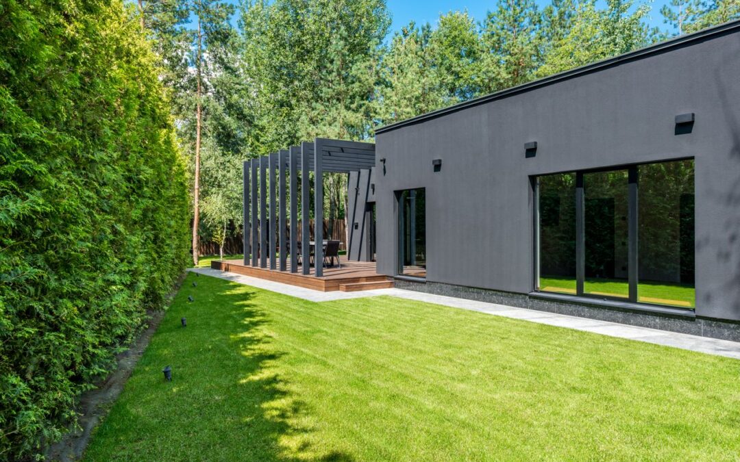 jardin d'une maison contemporaine aux murs sombres, dotée d'une terrasse en bois avec pergola et d'une pelouse soigneusement entretenue