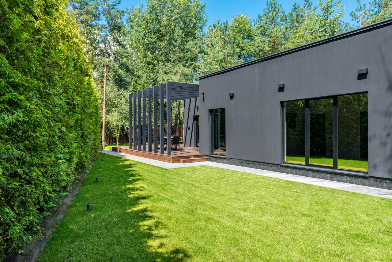 jardin d'une maison contemporaine aux murs sombres, dotée d'une terrasse en bois avec pergola et d'une pelouse soigneusement entretenue
