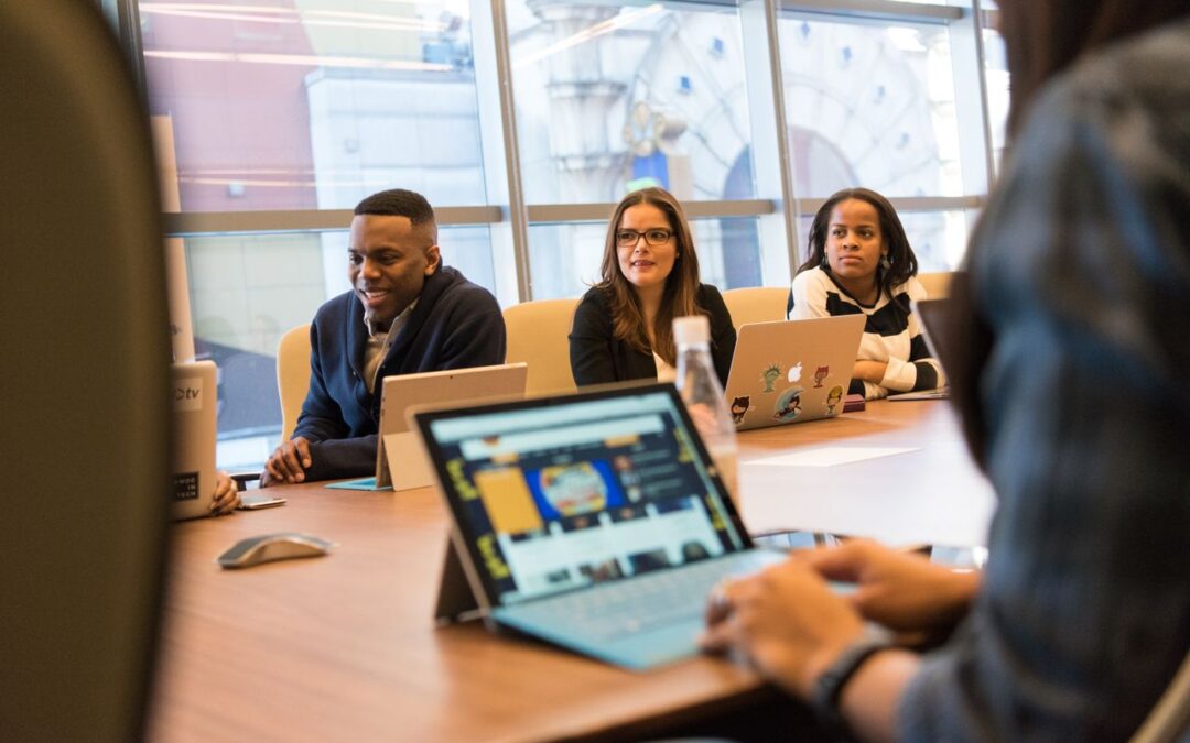 Une équipe professionnelle participant à une réunion de travail avec des ordinateurs portables autour d'une table dans une salle vitrée.
